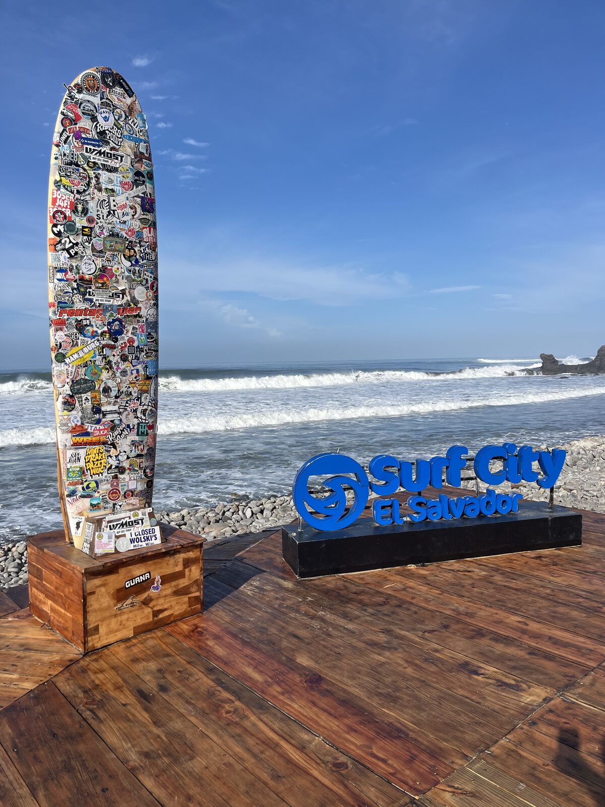 Surf City sign and sticker-covered longboard on the beach